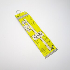 May include: A yellow and white cardboard package for a loop turner tool. The package features a drawing of a woman using the tool to make a loop in fabric. The text on the package reads "Loop Turner with Latch Hook" and "Turns tubing as small as 1/16 inch".