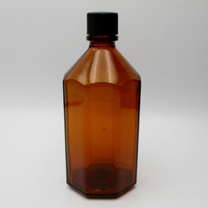 May include: A brown glass bottle with a black plastic lid. The bottle has a hexagonal shape and is empty.