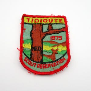 May include: Embroidered patch with a red border and a design featuring a tree, deer, and landscape. The patch has the words "Tidioute Scout Reservation" and the year "1979" in red and yellow lettering.