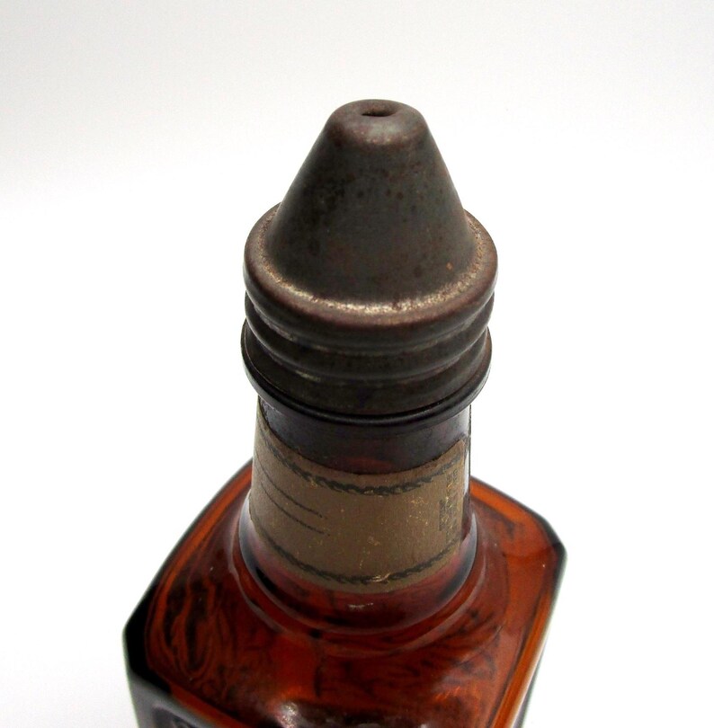 Puede incluir: Primer plano de la parte superior de una botella de vidrio &aacute;mbar con una tapa de metal. La tapa tiene un peque&ntilde;o agujero en la parte superior y est&aacute; ligeramente oxidada.