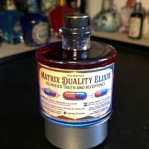 May include: A cylindrical glass bottle filled with a deep red liquid, topped with a dark stopper. The label reads Matrix Duality Elixir, Reunified Truth and Acceptance, featuring illustrations of red and blue capsules and detailed text.