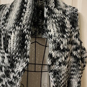 May include: A black and white knitted scarf with a chevron pattern. The scarf is draped over a black metal mannequin.