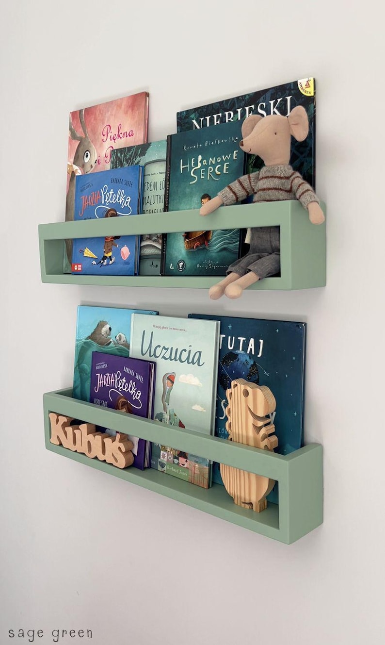 May include: Sage green floating bookshelves filled with children's books. A stuffed mouse sits on the top shelf. The bottom shelf has a wooden name cutout that says "Kubuś".
