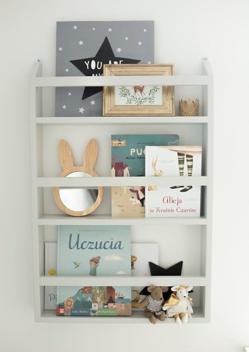 May include: A white bookshelf with five shelves, filled with children's books, a wooden bunny mirror, and a framed print with a star and the words "You are my".