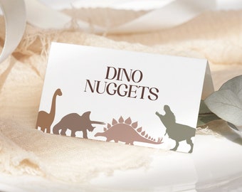 Może przedstawiać: Biała karta z tekstem "DINO NUGGETS" w brązowych literach. Karta jest ozdobiona brązowymi, różowymi i zielonymi sylwetkami dinozaurów.