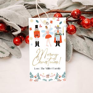 Könnte beinhalten: Ein weißer Weihnachtsgeschenkanhänger mit einer bunten Illustration eines Nussknackers, einer Ballerina und eines Mäusekönigs. Der Anhänger trägt den Text "Frohe Weihnachten!" und "Liebe, Die Familie Miller".