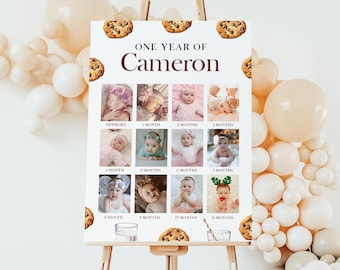 May include: A white poster board with a brown border and the text "ONE YEAR OF Cameron" in brown text. The poster board is divided into 12 squares, each with a photo of a baby at different ages. The photos are arranged in a grid pattern. The poster board is decorated with images of chocolate chip cookies.