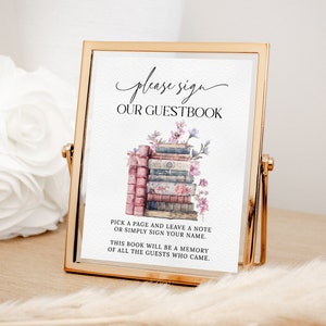 May include: A sign with the text "please sign our guestbook" and a watercolor illustration of a stack of books with flowers. The text below the image reads "Pick a page and leave a note or simply sign your name. This book will be a memory of all the guests who came."