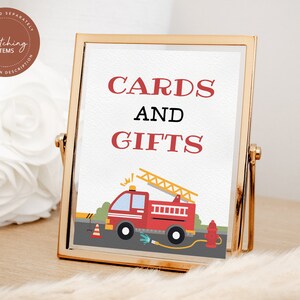 May include: A gold-framed sign with the text "CARDS AND GIFTS" in red letters. A cartoon fire truck with a ladder is pictured below the text.