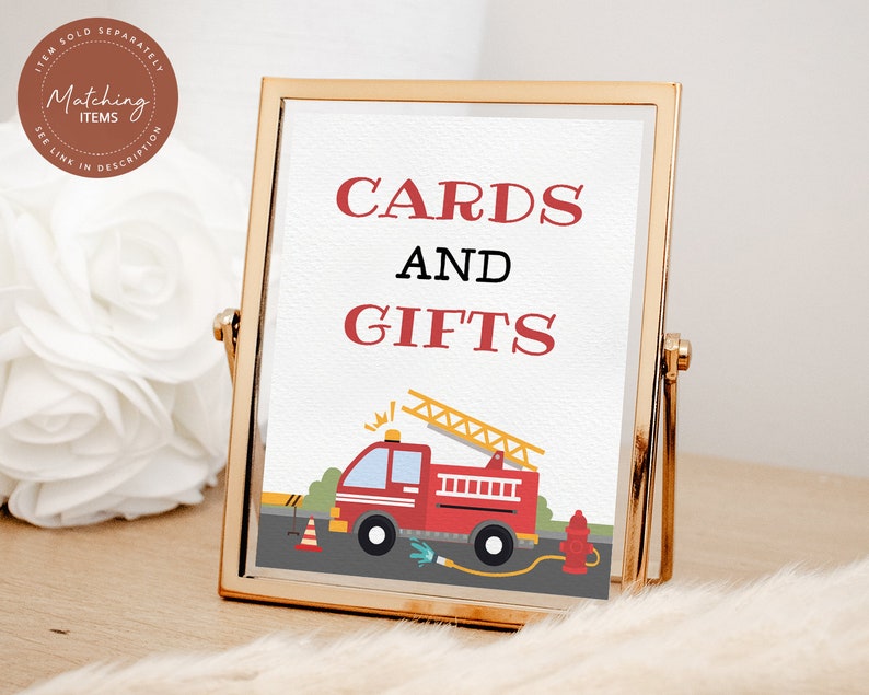 May include: A gold-framed sign with the text "CARDS AND GIFTS" in red letters. A cartoon fire truck with a ladder is pictured below the text.