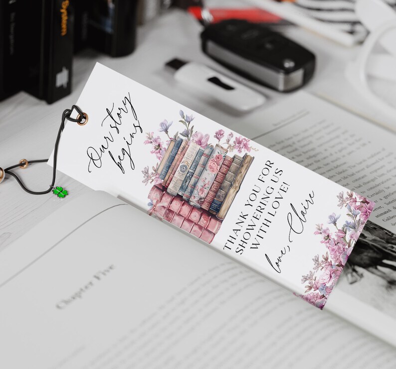 Op de afbeelding: Een witte bladwijzer met een stapel vintage boeken, roze bloemen en de tekst "Our story begins" en "Thank you for showering us with love! love, Claire".