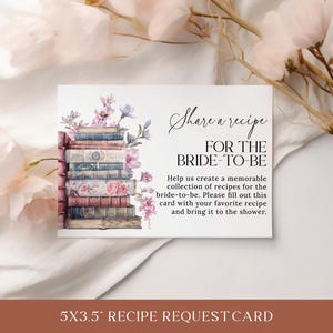 May include: A white card with a floral design and a stack of books. The text on the card reads "Share a recipe for the bride-to-be. Help us create a memorable collection of recipes for the bride-to-be. Please fill out this card with your favorite recipe and bring it to the shower."