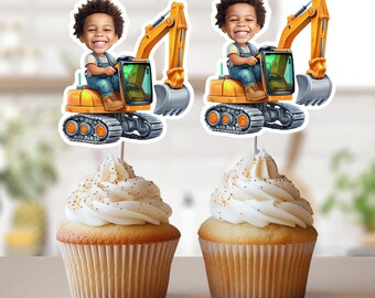 May include: Two yellow toy construction vehicles with a cartoon child driver on each. The vehicles are on cupcake toppers with white frosting and gold sprinkles.