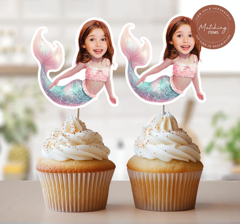May include: Two cupcakes topped with custom mermaid cake toppers featuring a child's face on a mermaid body with a pink ruffled top and a shimmering iridescent tail. A circular brown badge in the corner contains the text Matching Items.