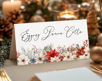 May include: A white place card with a floral design featuring red poinsettias, white flowers, and green leaves. The text "Eggnog Panna Cotta" is written in black cursive script.