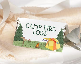 May include: A white folded card with the text CAMP FIRE LOGS in dark green. The illustration features a green forest, a wooden signpost, a small campfire, and a yellow and orange tent with colourful bunting flags against a grassy landscape.