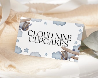 Może przedstawiać: Biała karta z wzorem niebieskiego i białego samolotu i chmur. Tekst "Cloud Nine Cupcakes" jest wydrukowany czarnym kolorem.