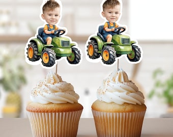 May include: Two green toy tractors with a cartoon boy driving each one. The tractors are on cupcake toppers with white frosting and gold sprinkles.