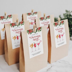 Op de afbeelding: Bruine papieren cadeauzakken met kaartjes waarop "Geniet van de kerstsfeer" staat en een aquarelillustratie van cocktails. De kaartjes bevatten ook de namen "Love, Ray & Georgina Smith-Anderson".