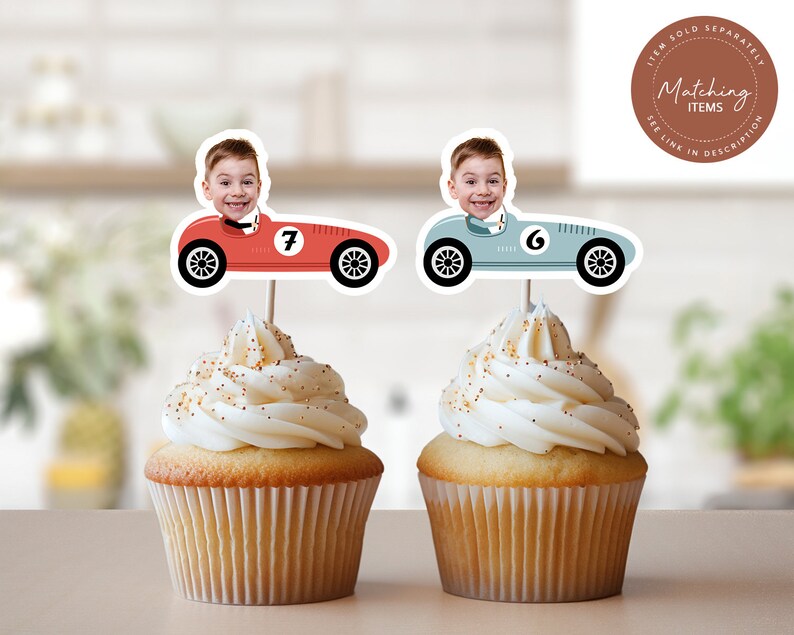 May include: Two cupcake toppers featuring a red and a blue racing car with a boy's face in the driver's seat. The red car has the number 7 on it and the blue car has the number 6 on it. The toppers are on top of cupcakes with white frosting.