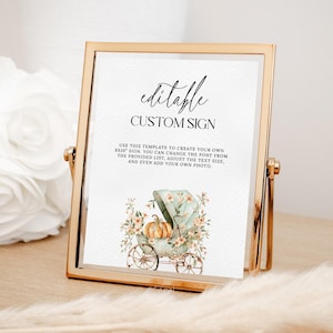 May include: A gold-framed sign with the words "editable CUSTOM SIGN" in black script. The sign includes a watercolor illustration of a baby carriage with a pumpkin and floral accents. The text below explains how to customize the sign.