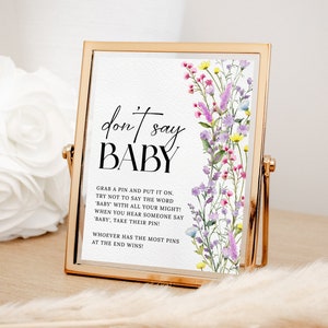 May include: A white card with a floral design and the text "don't say BABY" in black. The card also includes instructions for a game: "Grab a pin and put it on. Try not to say the word 'baby' with all your might! When you hear someone say 'baby', take their pin! Whoever has the most pins at the end wins!"