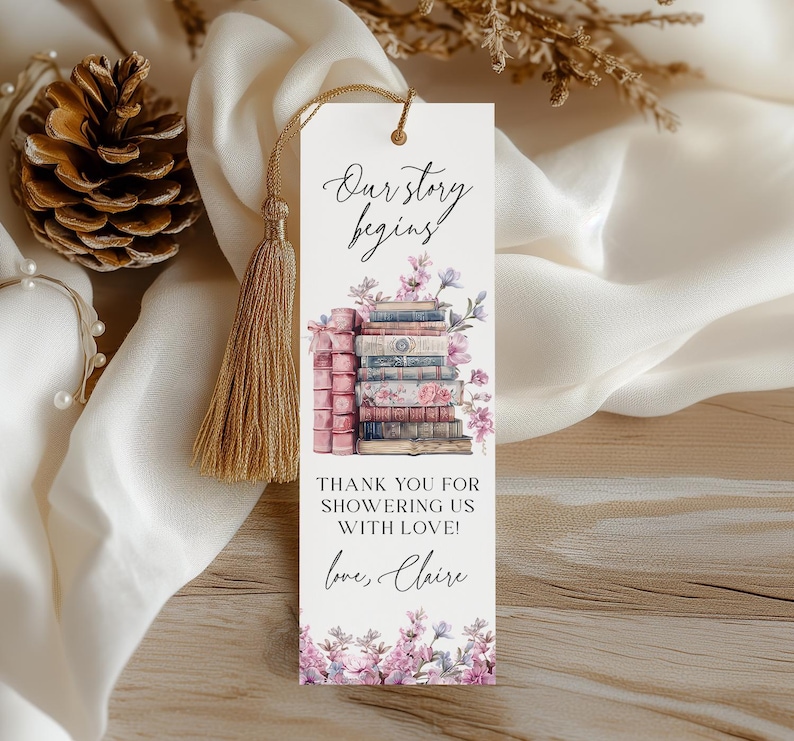 Op de afbeelding: Een witte bladwijzer met een stapel antieke boeken, roze bloemen en de tekst "Our story begins! Thank you for showering us with love! Love, Claire".