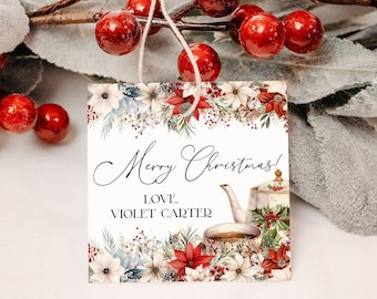 May include: A square Christmas gift tag with floral and teapot illustrations. The tag features the text "Merry Christmas! Love, Violet Carter." The tag is adorned with red poinsettias, white flowers, and green foliage. A string is attached for hanging.