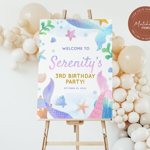 May include: A welcome sign for a 3rd birthday party with a mermaid theme. The sign is decorated with watercolor illustrations of mermaids, seashells, and starfish. The text on the sign reads "Welcome to Serenity's 3rd Birthday Party! October 23, 20XX".