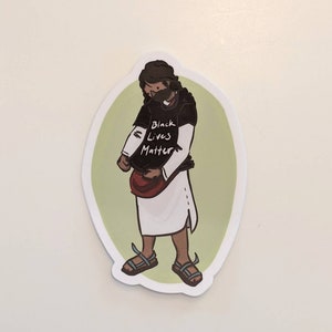 Puede incluir: Una pegatina de una persona de dibujos animados que lleva una camiseta negra con el texto "Black Lives Matter" y una t&uacute;nica blanca. La persona lleva una mascarilla y sandalias.