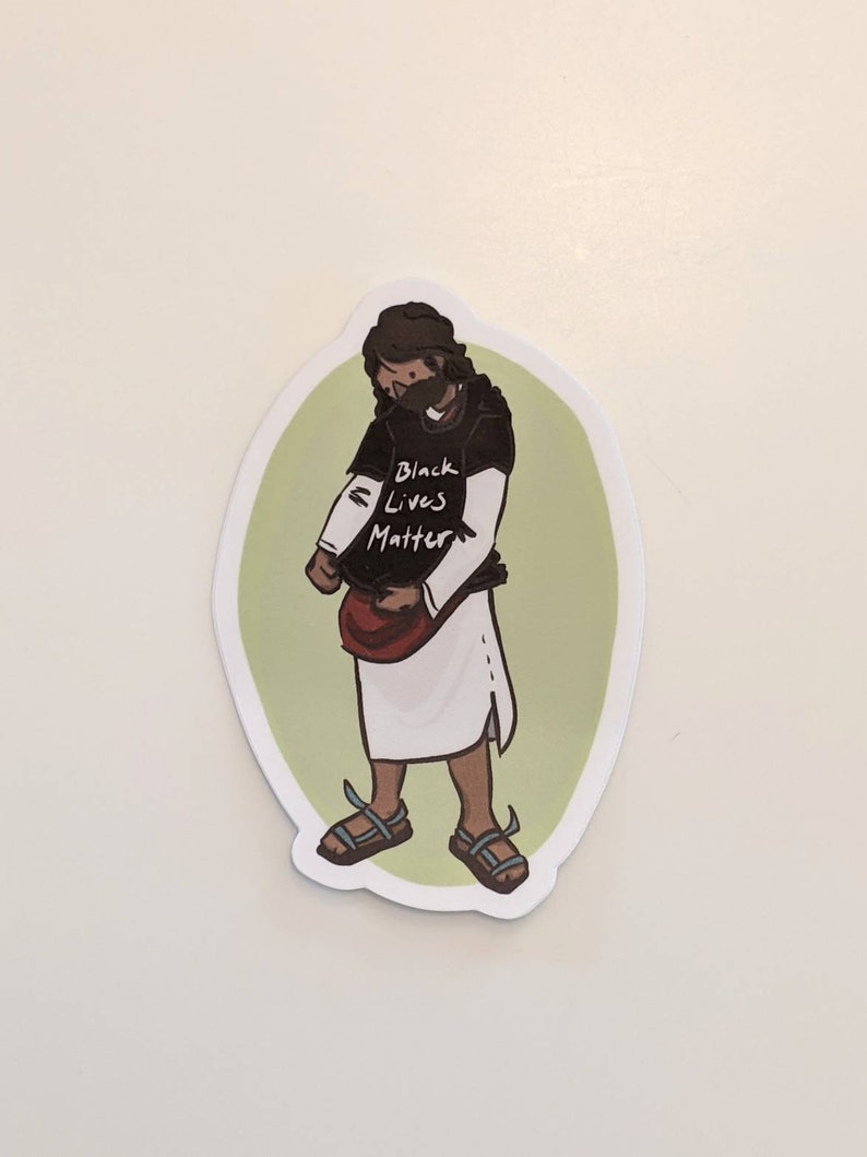 Puede incluir: Una pegatina de una persona de dibujos animados que lleva una camiseta negra con el texto "Black Lives Matter" y una t&uacute;nica blanca. La persona lleva una mascarilla y sandalias.