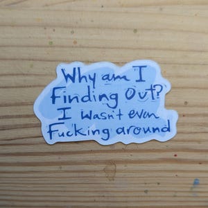 Pode incluir: Um autocolante azul claro com o texto "Why am I Finding Out? I wasn't even Fucking around" em azul escuro. O autocolante est&aacute; numa superf&iacute;cie de madeira.