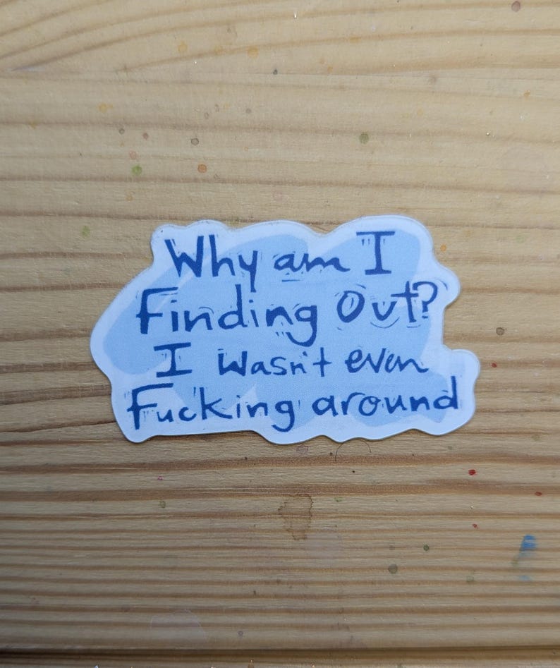 Pode incluir: Um autocolante azul claro com o texto "Why am I Finding Out? I wasn't even Fucking around" em azul escuro. O autocolante est&aacute; numa superf&iacute;cie de madeira.