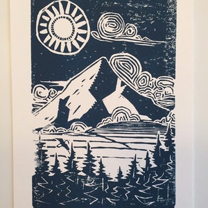 May include: A blue and white linocut print of a mountain scene with a sun, clouds, trees, and the text "Hood Winked" signed and numbered 4/4.
