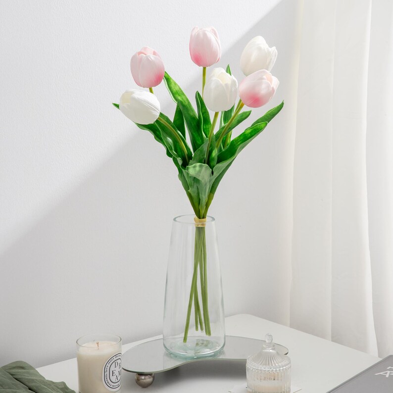 May include: A bouquet of artificial tulips in a clear glass vase. The tulips are a mix of white and pink.