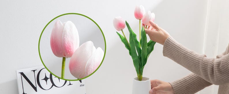 May include: A bouquet of pink artificial tulips with green leaves in a white vase. The tulips have a soft, velvety texture.