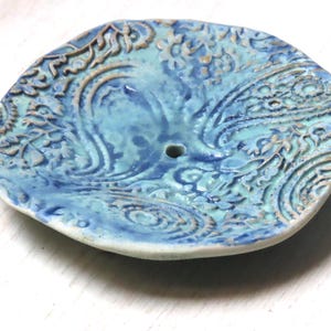 May include: A blue and white ceramic dish with a paisley pattern. The dish has a small hole in the center.