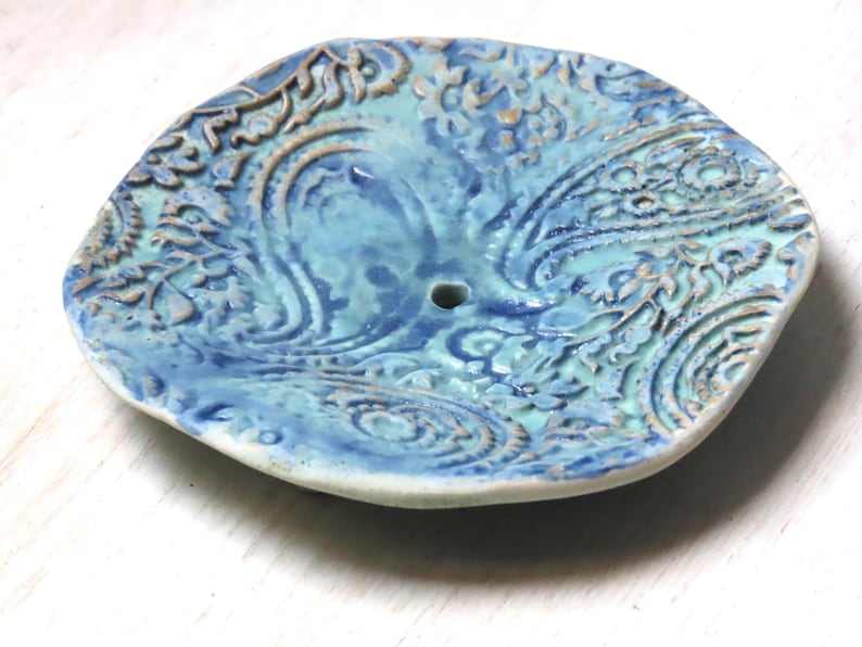 May include: A blue and white ceramic dish with a paisley pattern. The dish has a small hole in the center.