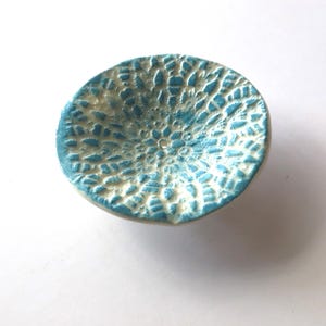 May include: A small, round ceramic bowl with a textured surface. The bowl is primarily light blue with a white, lace-like pattern. The bowl is a decorative item, likely for holding small items.