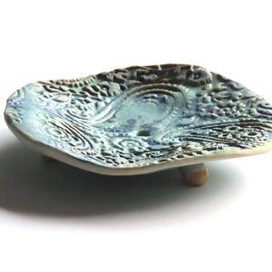 May include: A blue and green ceramic soap dish with a raised, textured design. The dish has three small feet and is shaped like a leaf.