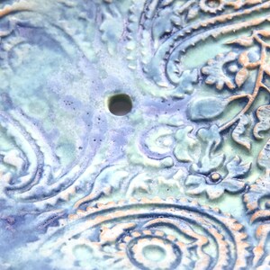 May include: A ceramic dish with a blue and green paisley pattern. The dish has a small hole in the center.