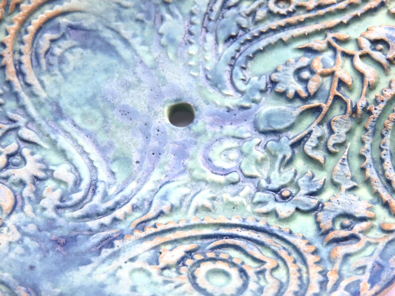 May include: A ceramic dish with a blue and green paisley pattern. The dish has a small hole in the center.