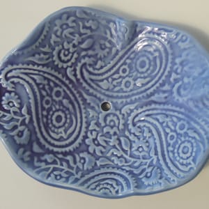 May include: A blue ceramic soap dish with a paisley pattern. The dish has a slightly irregular shape and a small drainage hole in the centre.