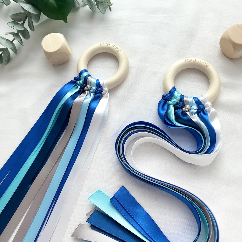 Puede incluir: Dos sonajeros para beb&eacute;s con aros de madera y cintas de raso azules, plateadas y blancas. Los aros tienen grabado "Pishu Baby". Tambi&eacute;n hay dos peque&ntilde;os cubos de madera.