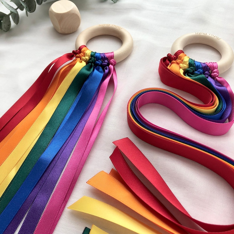 A smooth wooden ring with knotted ribbons used as a sensory gym toy for babies. The ribbons come in two different lengths; 21cm or 42cm. You can also choose from five colour options: rainbow, pastel rainbow, monochrome, pink, or blue.