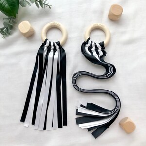 Puede incluir: Dos juguetes sensoriales para beb&eacute;s con aros de madera y cintas blancas y negras. Los aros tienen grabado el texto "Pishu Baby". Las cintas son una mezcla de blanco y negro. Tambi&eacute;n hay tres peque&ntilde;os bloques de madera.
