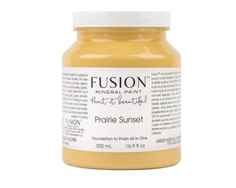 May include: A jar of Fusion Mineral Paint in the color "Prairie Sunset." The jar is filled with a warm, yellow-orange paint and has a white lid. The label includes the text "Paint it beautiful" and "Foundation to Finish All In One."