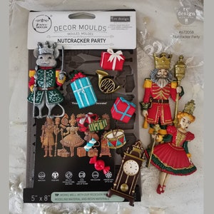 May include: A silicone mold for making nutcracker themed decorations. The mold features a nutcracker soldier, a mouse soldier, a ballerina, a clock, a drum, presents, and a candy cane. The mold is 5 inches by 8 inches.