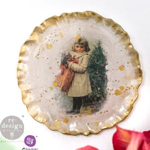 May include: A round decorative plate with a scalloped, gold-painted edge. The center features a vintage-style illustration of a child in a beige coat holding a bag next to a Christmas tree. Gold paint splatters decorate the surface of the plate.