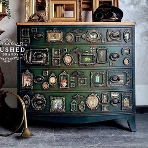 May include: A dark green dresser with a curved front and ornate gold accents. The dresser is decorated with small framed pictures and other decorative elements. The dresser is sitting in front of a wall with a textured finish.